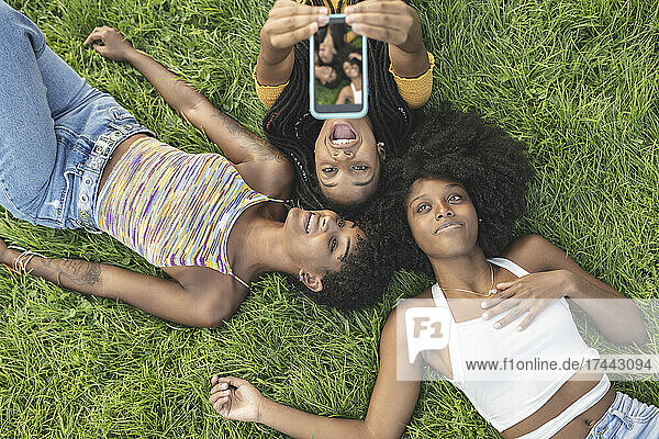 Fröhliche Frau macht ein Selfie per Handy mit Freundinnen im Gras