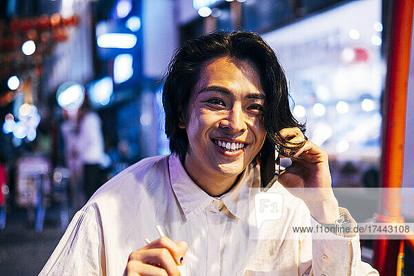 Happy young man talking on mobile phone in illuminated city