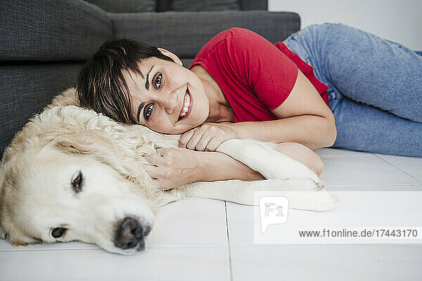 Smiling mid adult woman lying with dog on floor at home