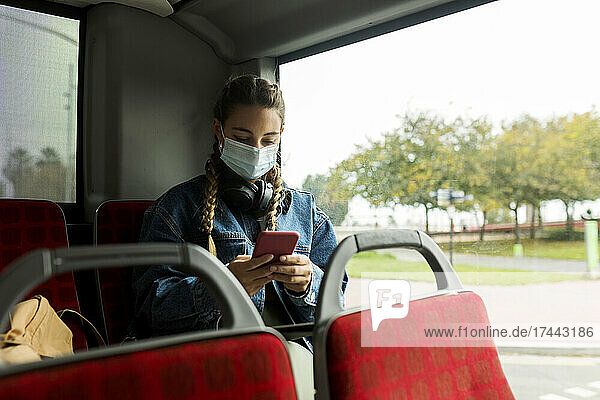 Frau trägt Schutzmaske und benutzt Smartphone im Bus