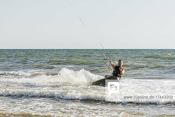 Man with surfboard kiteboarding on sea during sunny day