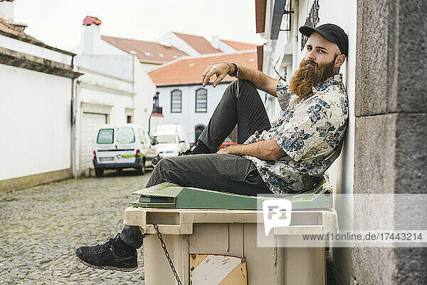 Bearded man sitting on garbage bin