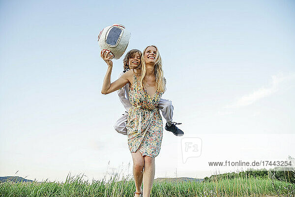 Verspielte Mutter gibt ihrem Sohn eine Huckepackfahrt  während sie auf dem Gras läuft