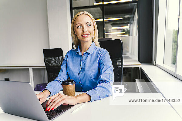 Blonde Geschäftsfrau mit Laptop sitzt am Schreibtisch im Büro