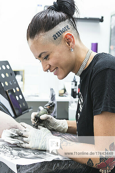 Smiling female artist tattooing on male customer's arm in studio