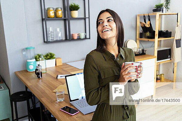 Happy female freelancer holding coffee mug at home