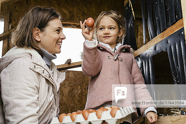 Smiling mid adult woman looking at daughter holding egg