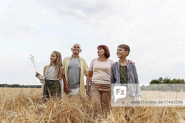Siblings walking with grandparents on wheat field
