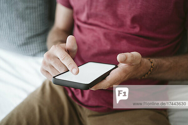 Mid adult man touching screen while using smart phone at home