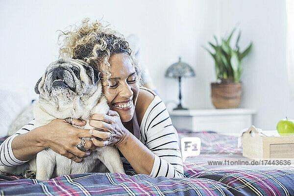 Happy woman embracing pug on bed at home