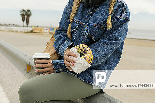 Frau mit Donut und Kaffee sitzt auf dem Geländer