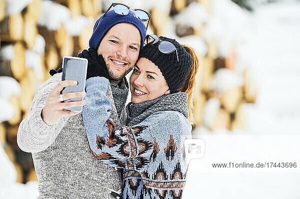 Couple in knit hats taking selfie through smart phone during winter