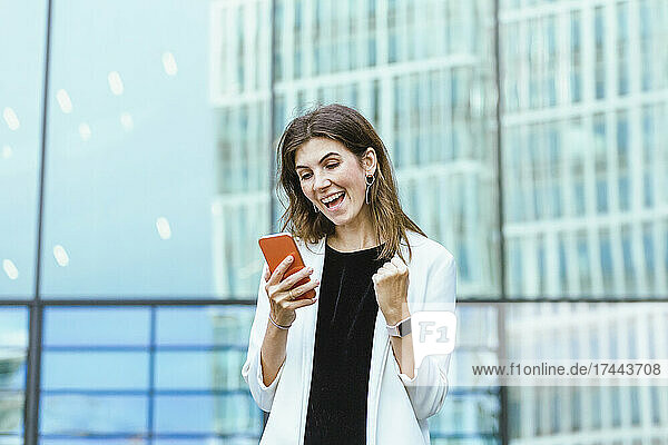 Happy female professional gesturing fist while using mobile phone