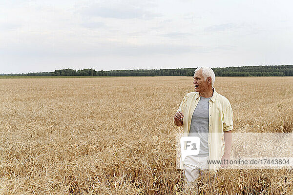 Smiling senior man standing on wheat field