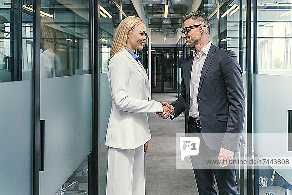 Businessman greeting female colleague in corridor at office