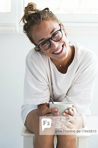 Beautiful woman wearing eyeglasses holding mug while sitting at home