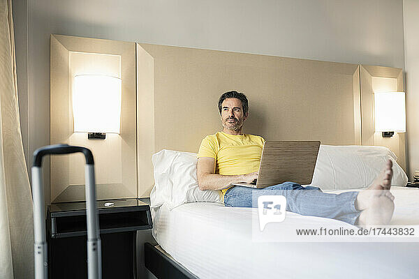 Mature male professional with laptop on bed in hotel room