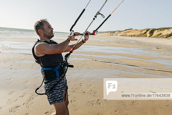 Mid adult man kiteboarding on beach during sunny day