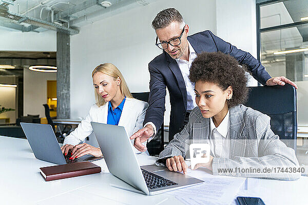 Male business professional explaining female colleague over laptop at desk