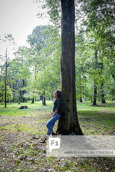 Woman leaning on tree trunk at park