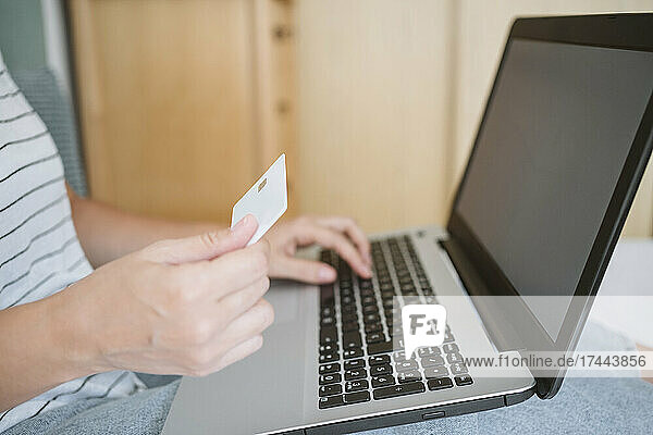 Woman holding credit card while using laptop at home