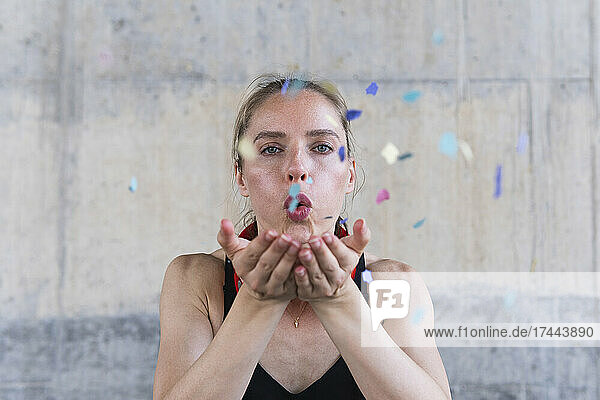 Female athlete blowing confetti in front of wall