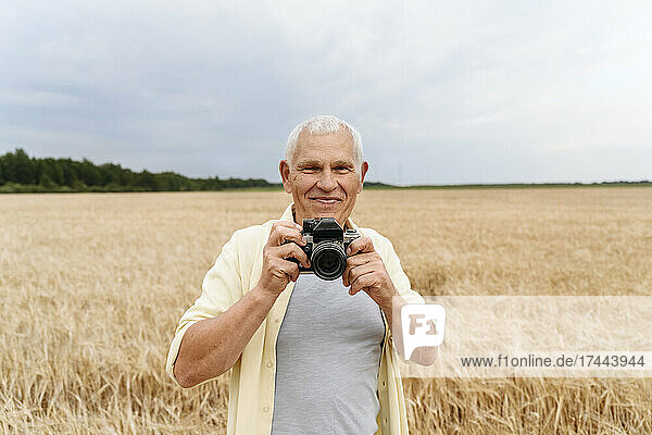 Smiling senior man holding camera at agricultural field