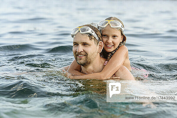 Father giving piggyback ride to daughter while swimming in sea
