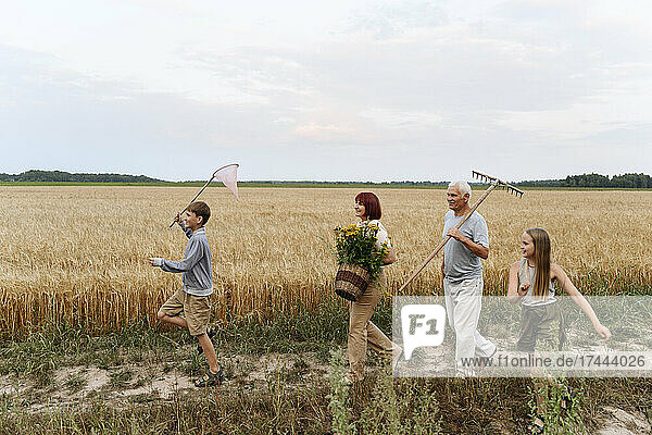 Playful children walking with grandparents on field