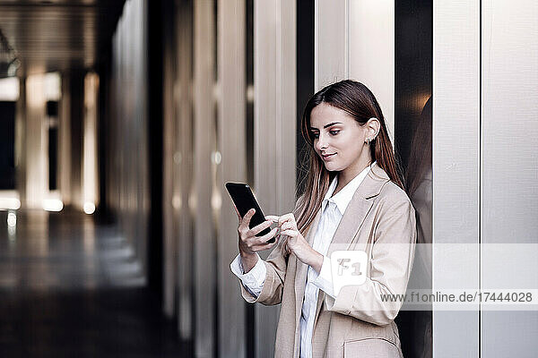 Female professional surfing net through mobile phone while standing at corridor