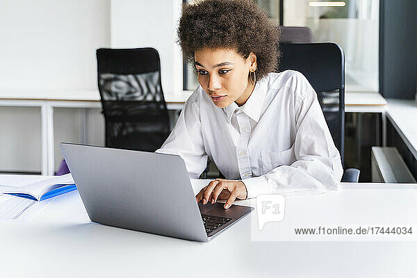 Young female professional using laptop at desk in office