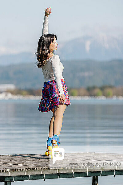 Carefree mature woman with hand raised roller skating on pier