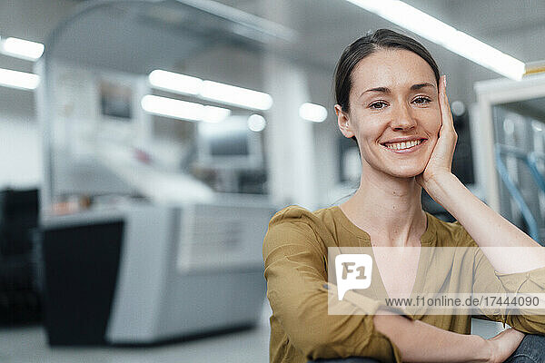 Glückliche Geschäftsfrau mit der Hand am Kinn sitzt in der Werkstatt