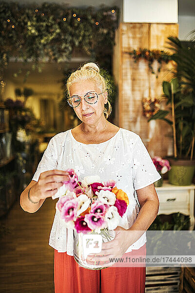 Reife Floristin arrangiert Blumen in einer Vase im Geschäft
