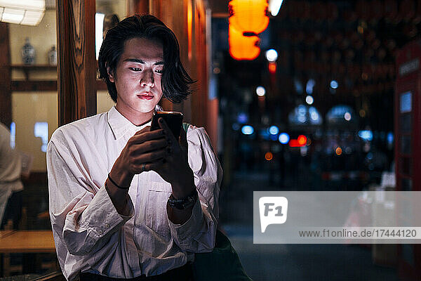 Young man with black hair using smart phone in city at night