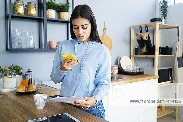 Frau fotografiert Dokument mit Mobiltelefon am Küchentisch
