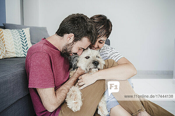 Mid adult couple embracing dog while sitting at home