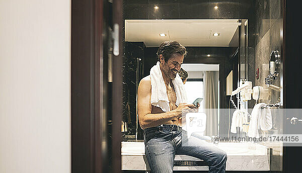 Smiling man using mobile phone on sink in hotel room