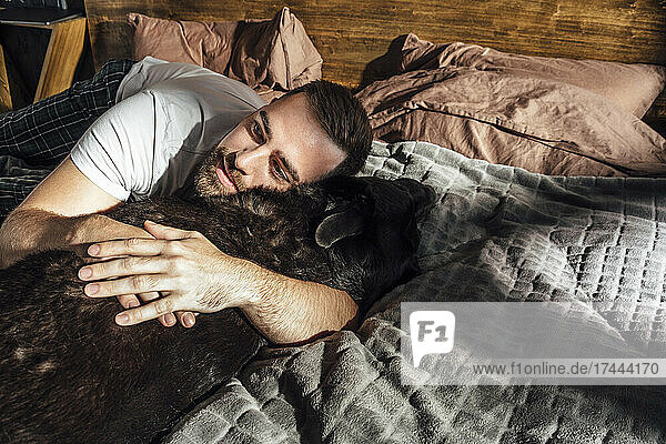 Mitte erwachsener Mann umarmt Hund auf dem Bett