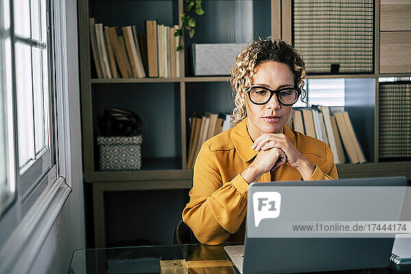 Female freelancer with hand on chin looking at laptop