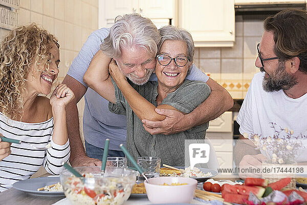 Senior woman embracing man while sitting with family at dining table