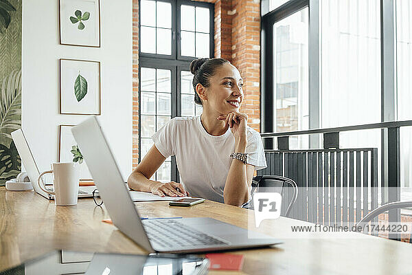 Thoughtful businesswoman with hand on chin sitting at desk