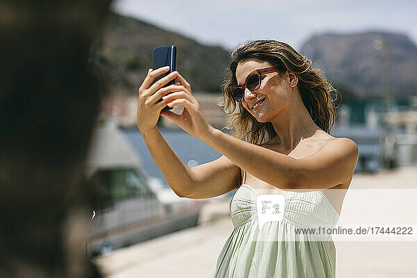 Smiling woman with sunglasses taking selfie through smart phone