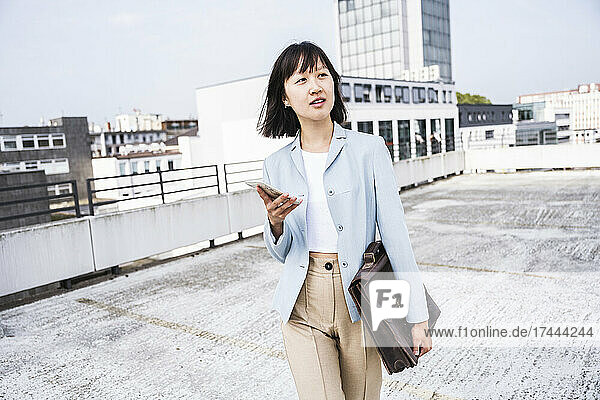 Female business professional with mobile phone and briefcase walking on rooftop