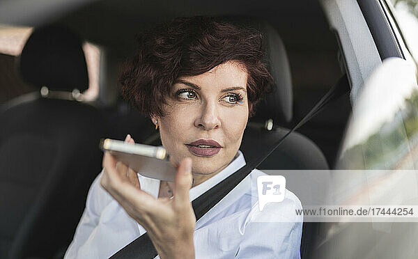 Female professional sending voicemail through smart phone while sitting in car