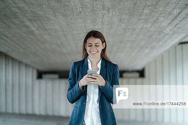 Smiling female freelancer surfing net through smart phone in basement