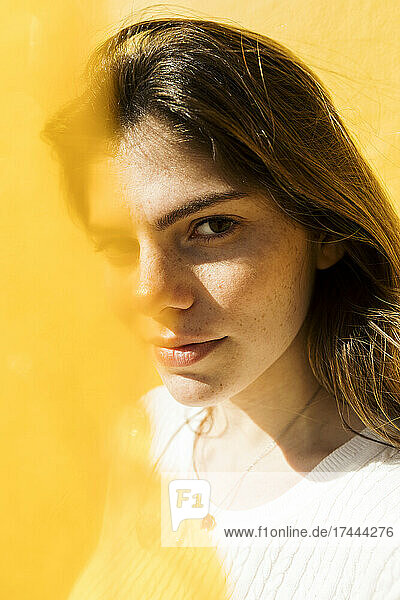 Junge Frau mit braunen Haaren vor gelber Wand an sonnigen Tagen