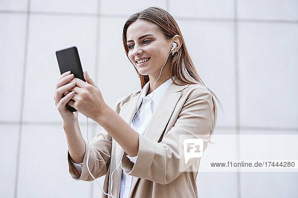 Businesswoman smiling while doing video call through smart phone in front of wall