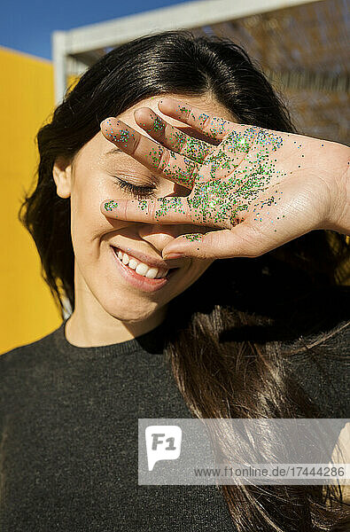 Smiling woman covering face with green glitter on palm