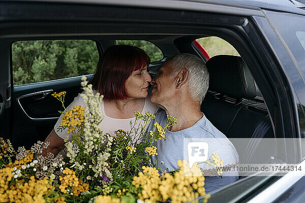 Romantic senior couple sitting with tansy flowers while kissing in car